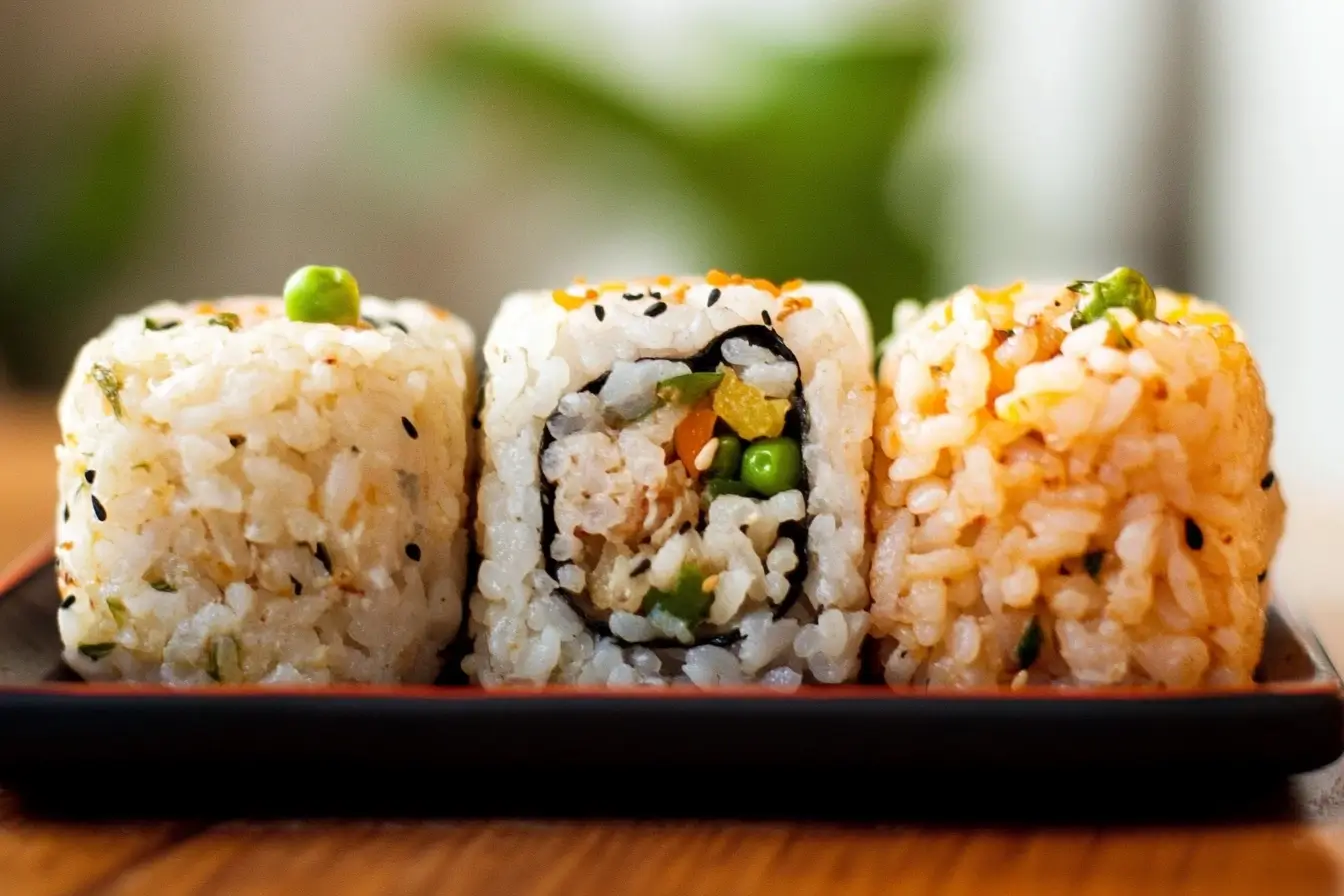 Three creatively styled rice portions, including sushi rolls and seasoned rice with peas and sesame seeds, highlighting diverse rice dish variations.