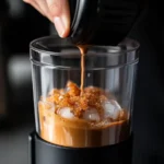 Hand shaking a cocktail shaker with espresso, ice, and brown sugar syrup in a warm kitchen setting, highlighting the frothy texture creation process.