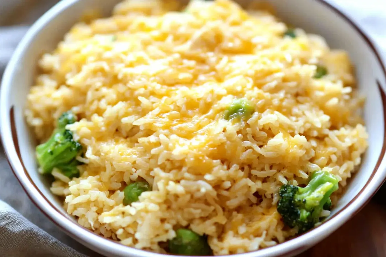 A bowl of cheesy rice with broccoli florets, featuring a creamy texture and golden melted cheese on top. The dish is served in a white ceramic bowl, offering a comforting and visually appealing meal.