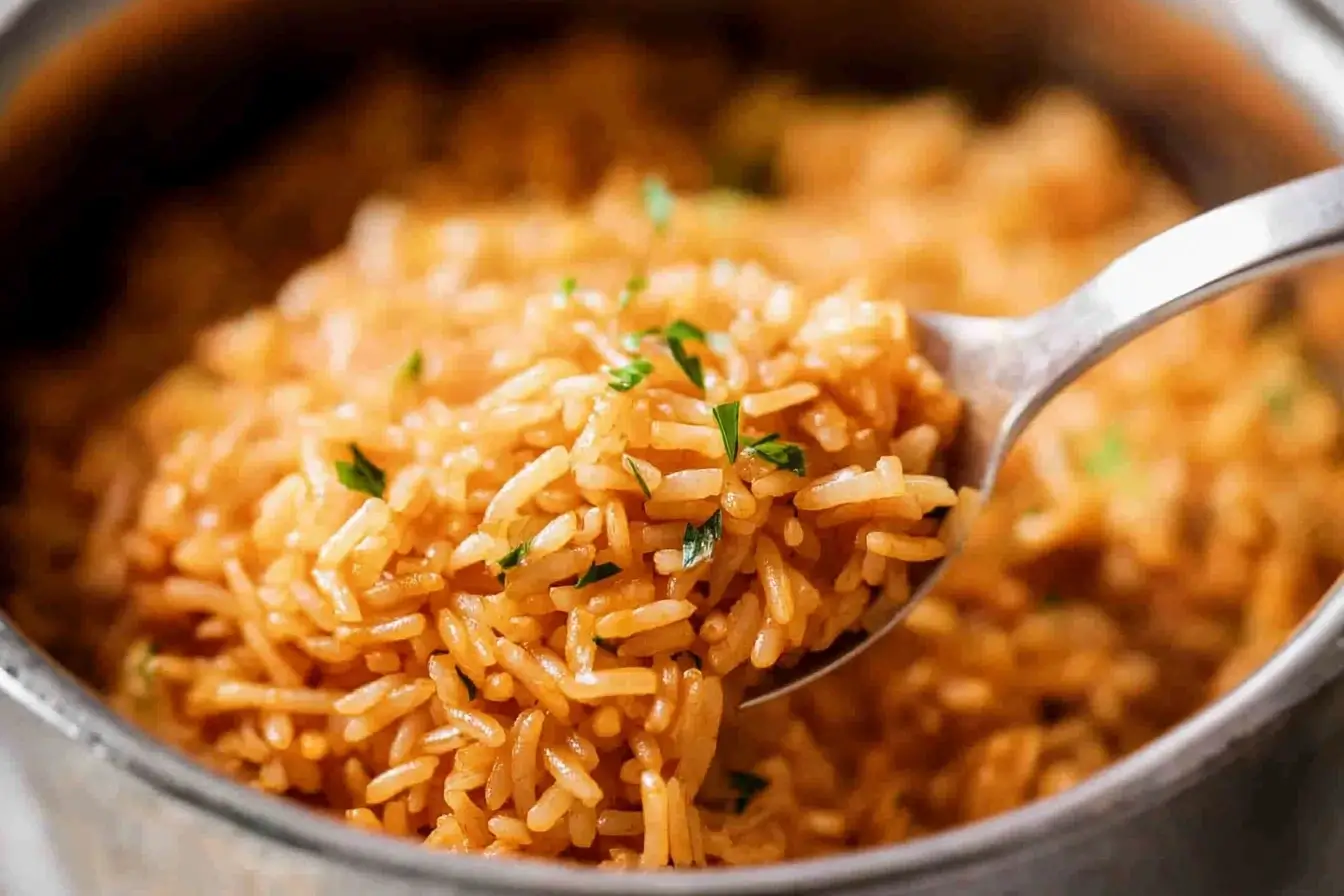 A close-up of cooked red rice being scooped with a spoon, garnished with fresh herbs, highlighting the fluffy texture and vibrant color.