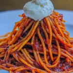 A beautifully plated tower of Spaghetti All’Assassina, topped with a dollop of creamy cheese, showcasing its caramelized tomato sauce and crispy texture.