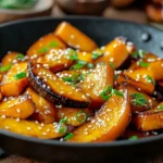 Stir-fried Kabocha squash wedges caramelized in garlic and ginger, garnished with sesame seeds and fresh green onions, served in a black wok.