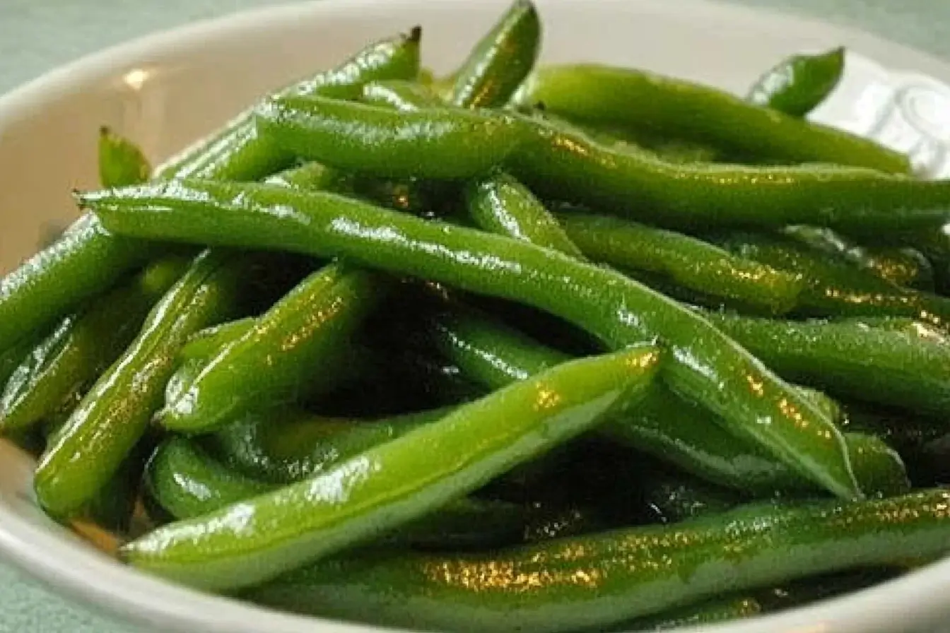 A close-up of freshly cooked green beans served in a white dish, showcasing their vibrant green color and glossy texture.