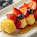 Mini pancake skewers with fluffy golden pancakes, fresh strawberries, blueberries, and a drizzle of maple syrup, served on a white plate for a vibrant breakfast presentation.