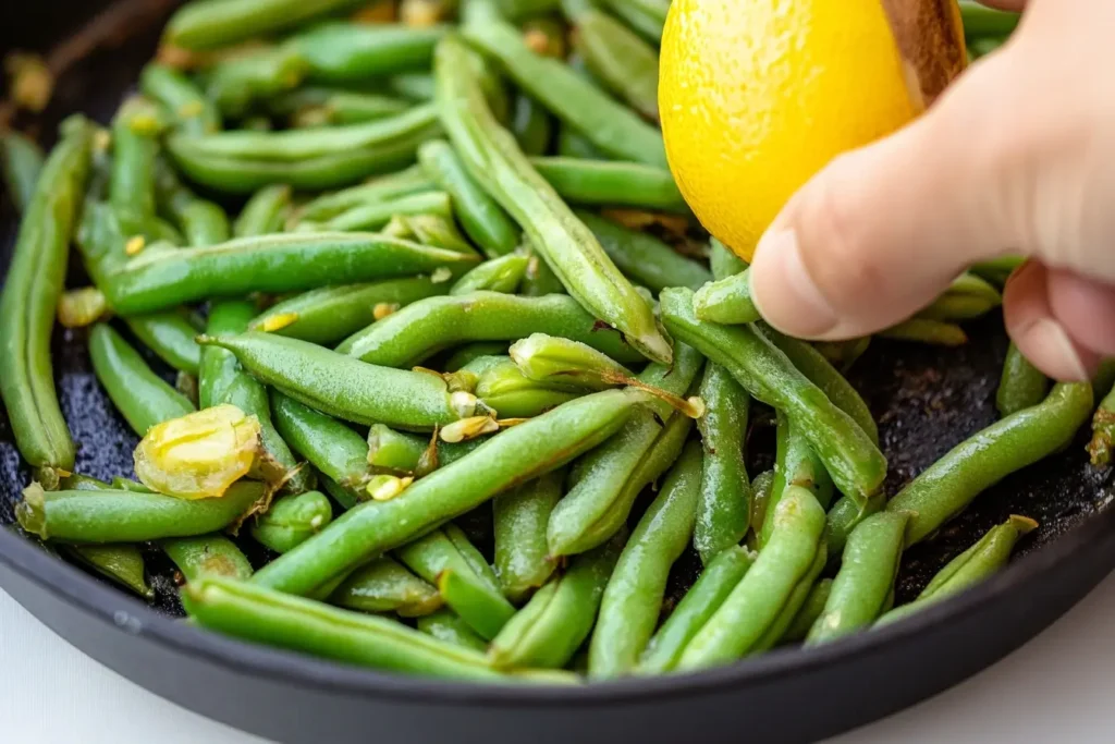 Fresh green beans being sautéed in a skillet with a hand squeezing a lemon for added flavor, showcasing vibrant colors and freshness.